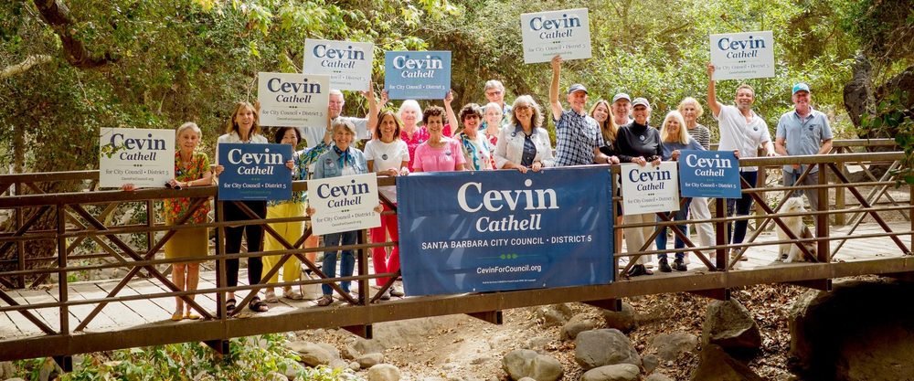 Cevin Cathell with more than twenty supporters holding campaign signs on a footbridge over a creek